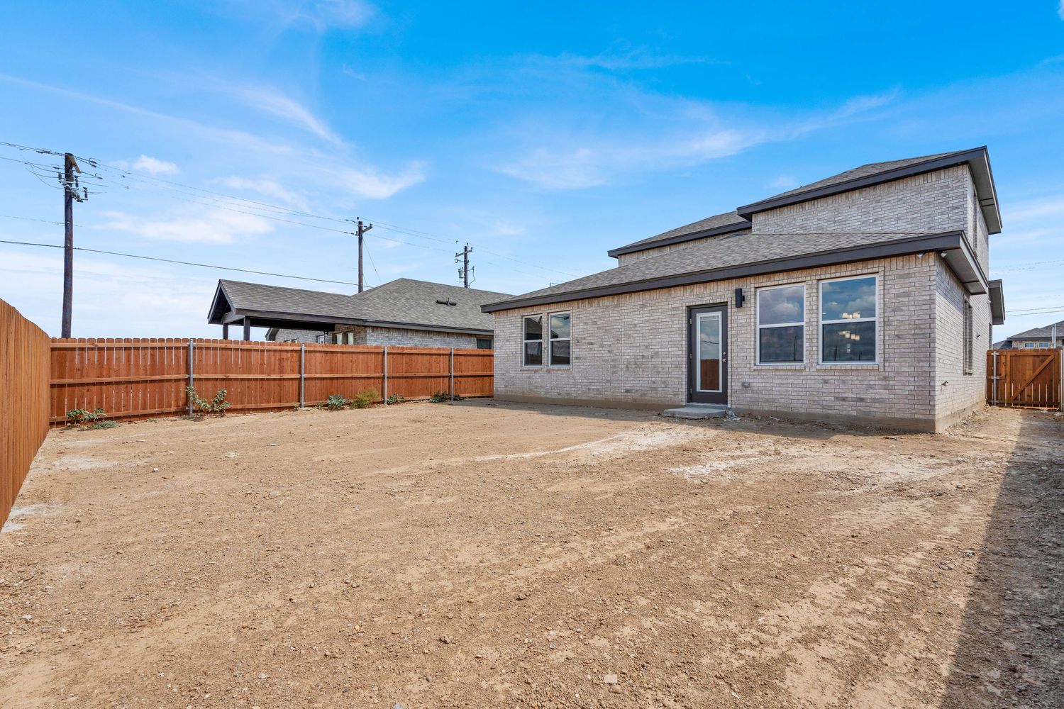 New construction home exterior with brick facade, large backyard, wood fence, and blue sky in a Texas suburb.