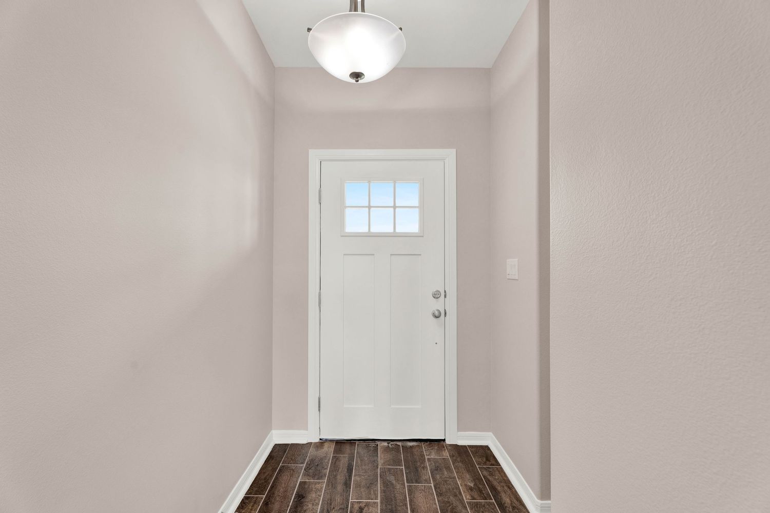 Bright entryway with white front door, small window, dark hardwood floors, and neutral gray walls.