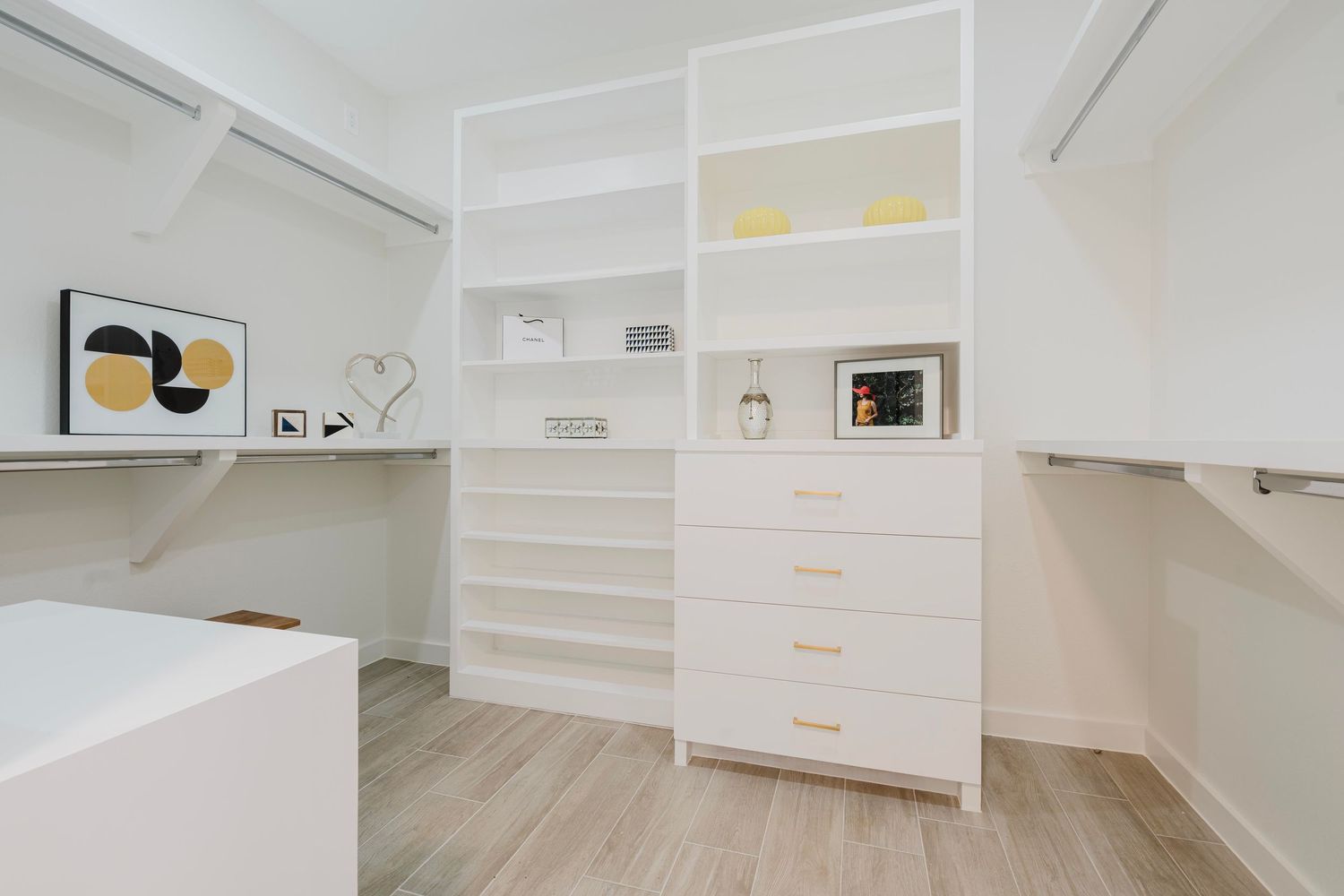 Organized walk-in closet featuring white cabinetry, open shelving, and geometric wall art.