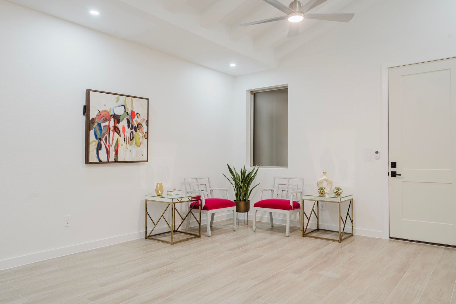 Contemporary seating area with colorful wall art, gold side tables, and red cushioned chairs on light wood floors.