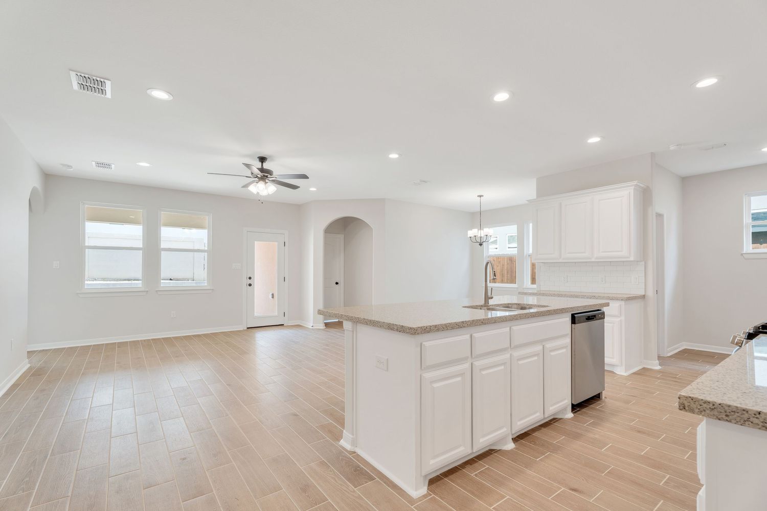 Modern open concept living space with white walls, wood flooring, and recessed lighting in a new construction home.