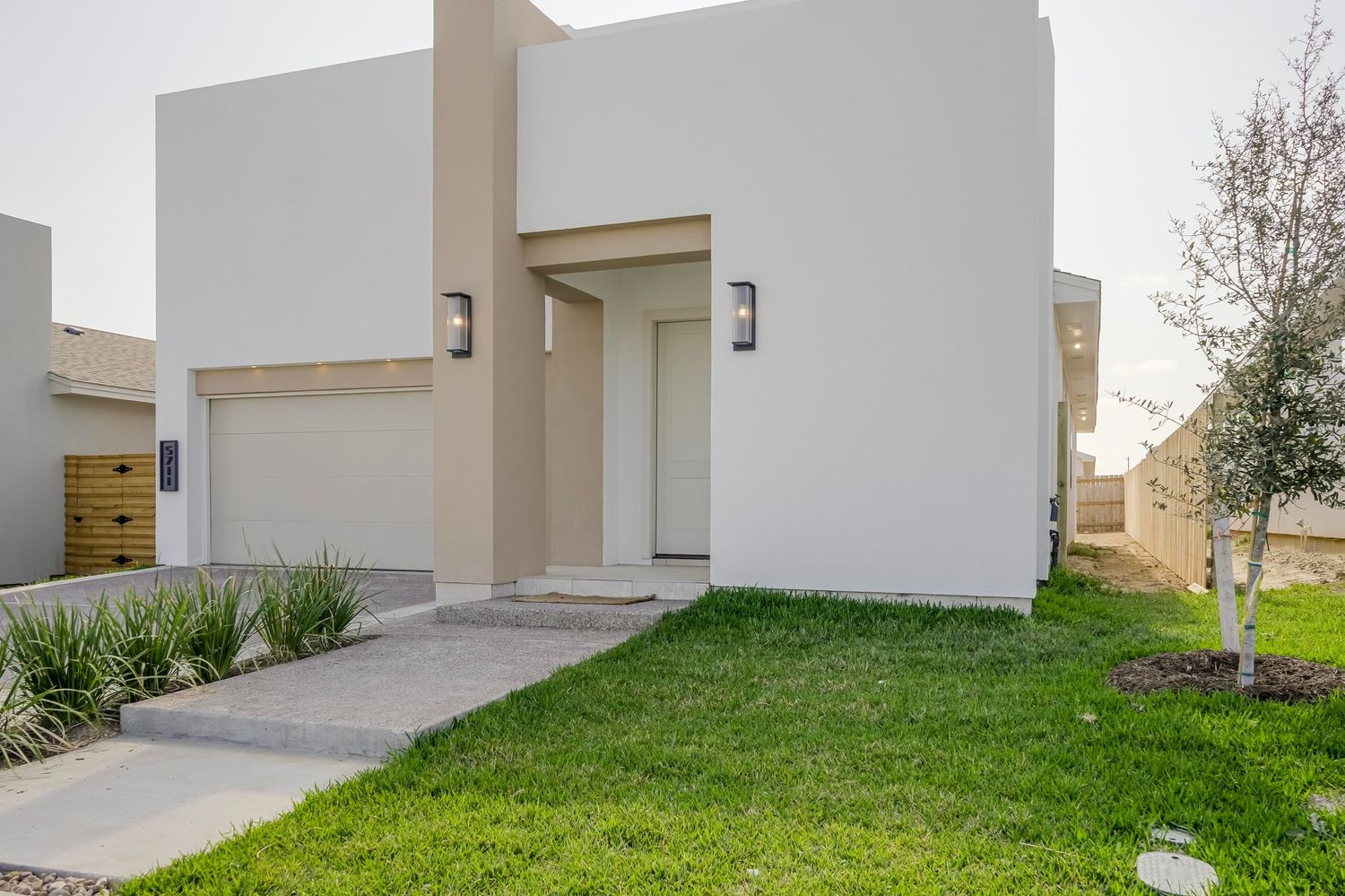 Contemporary white house exterior with manicured lawn and landscape lighting.