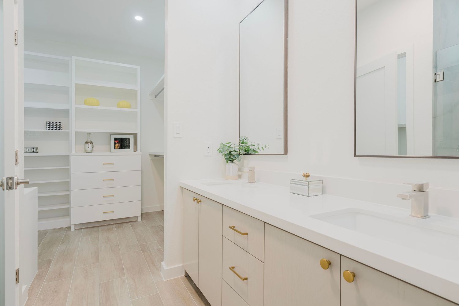 Modern white bathroom with double vanity, marble countertops, brass hardware, and built-in storage cabinetry.