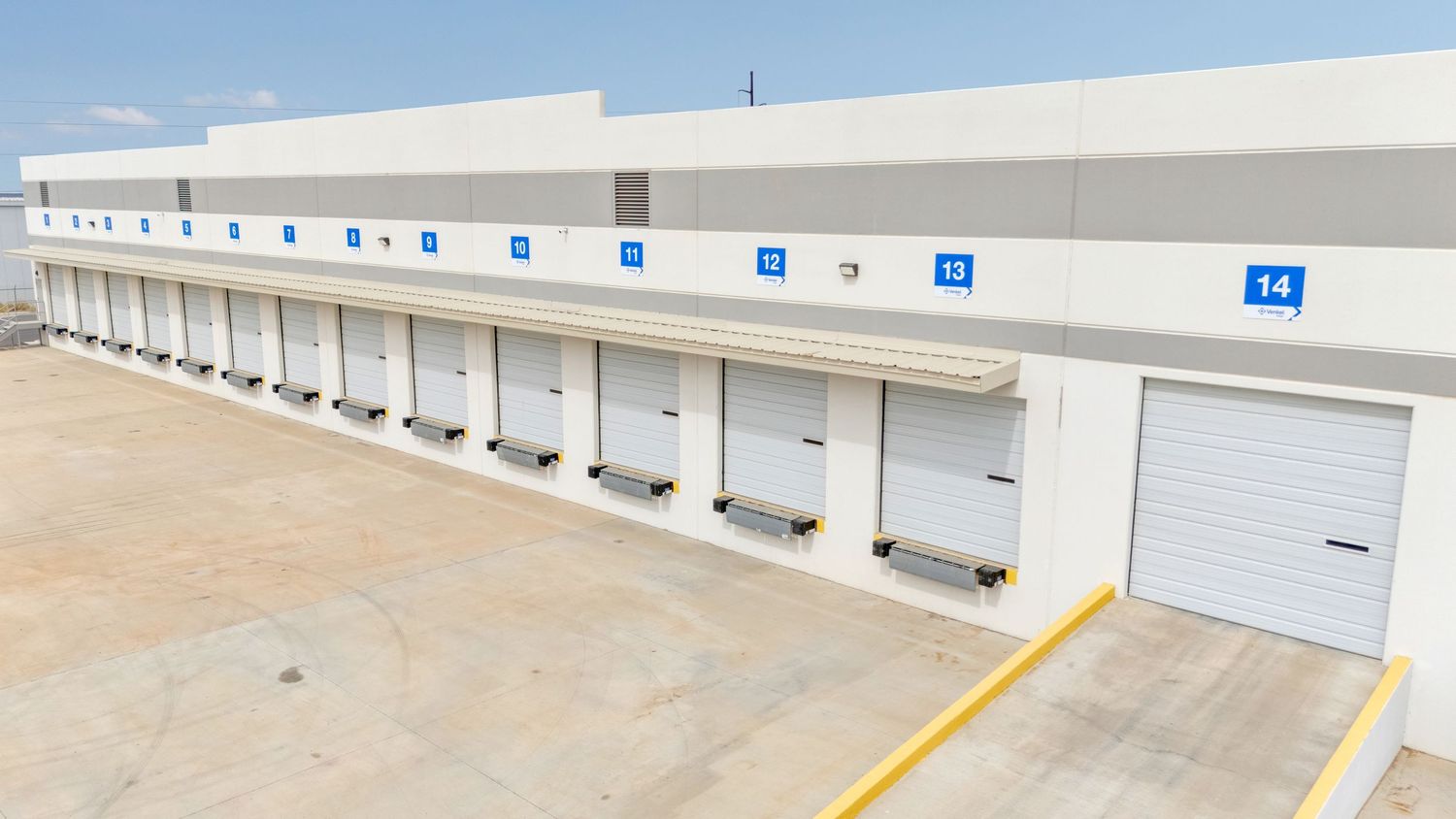 Modern loading dock with multiple white industrial garage doors and yellow safety lines painted on concrete floor.