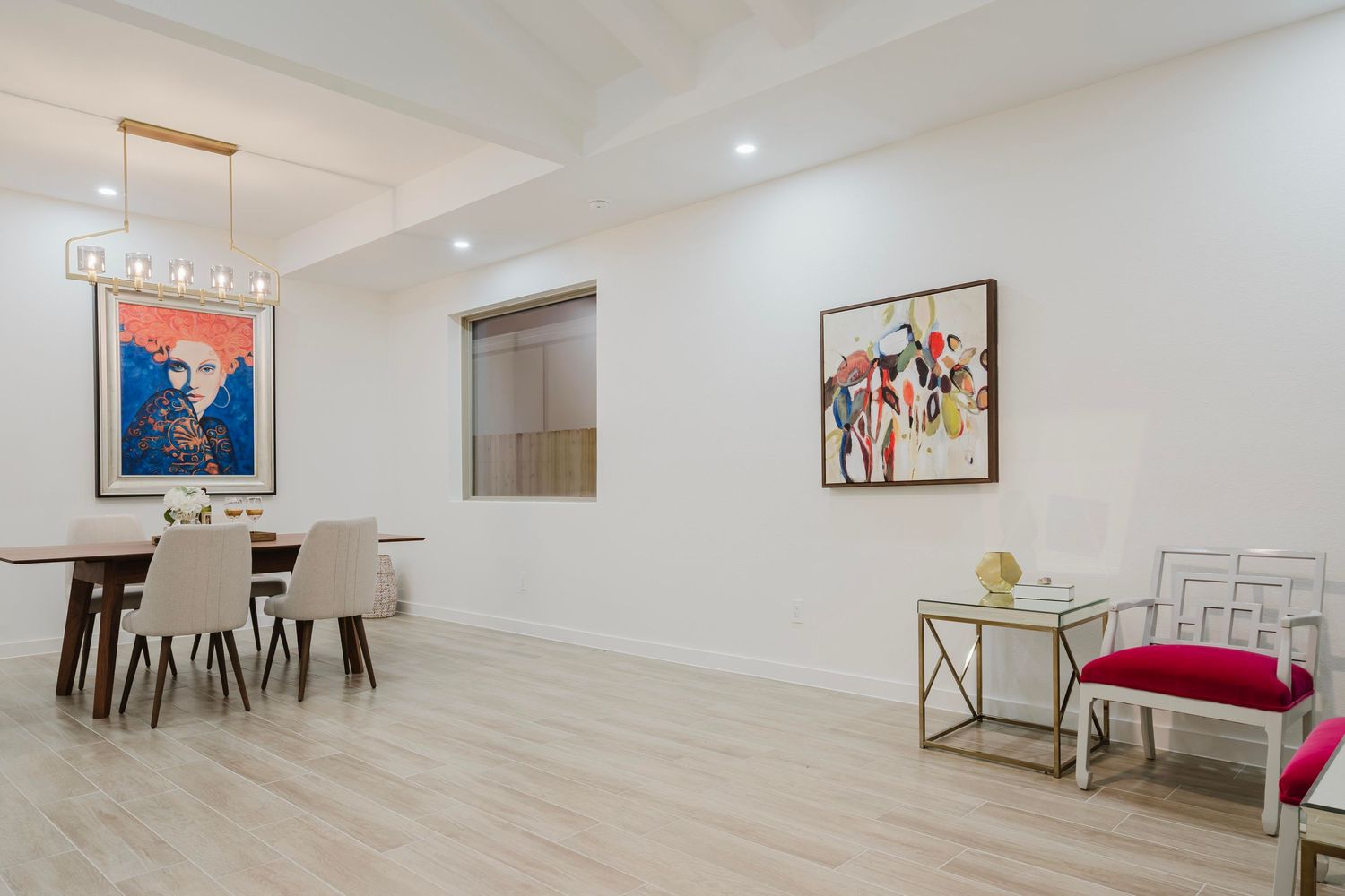 Modern dining room with white walls, wood flooring, and colorful artwork featuring sleek furniture and pendant lighting.