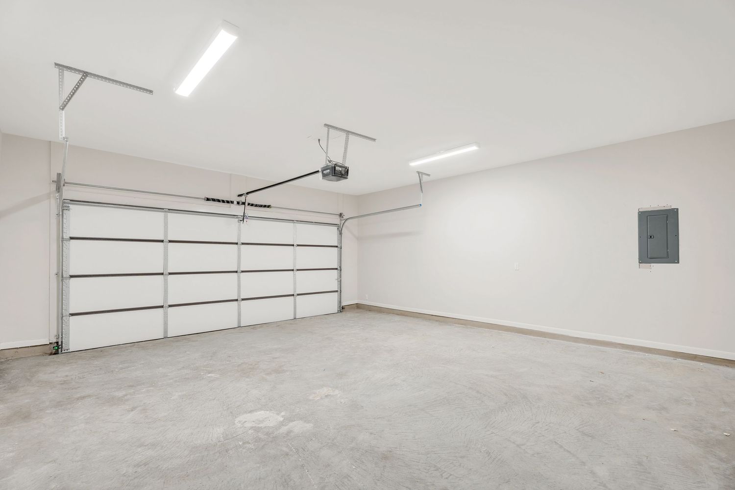 Empty white garage interior with concrete floor and fluorescent lighting mounted on ceiling.