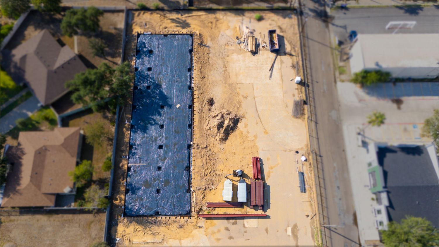 Aerial view of residential construction site showing foundation work and building materials in progress.