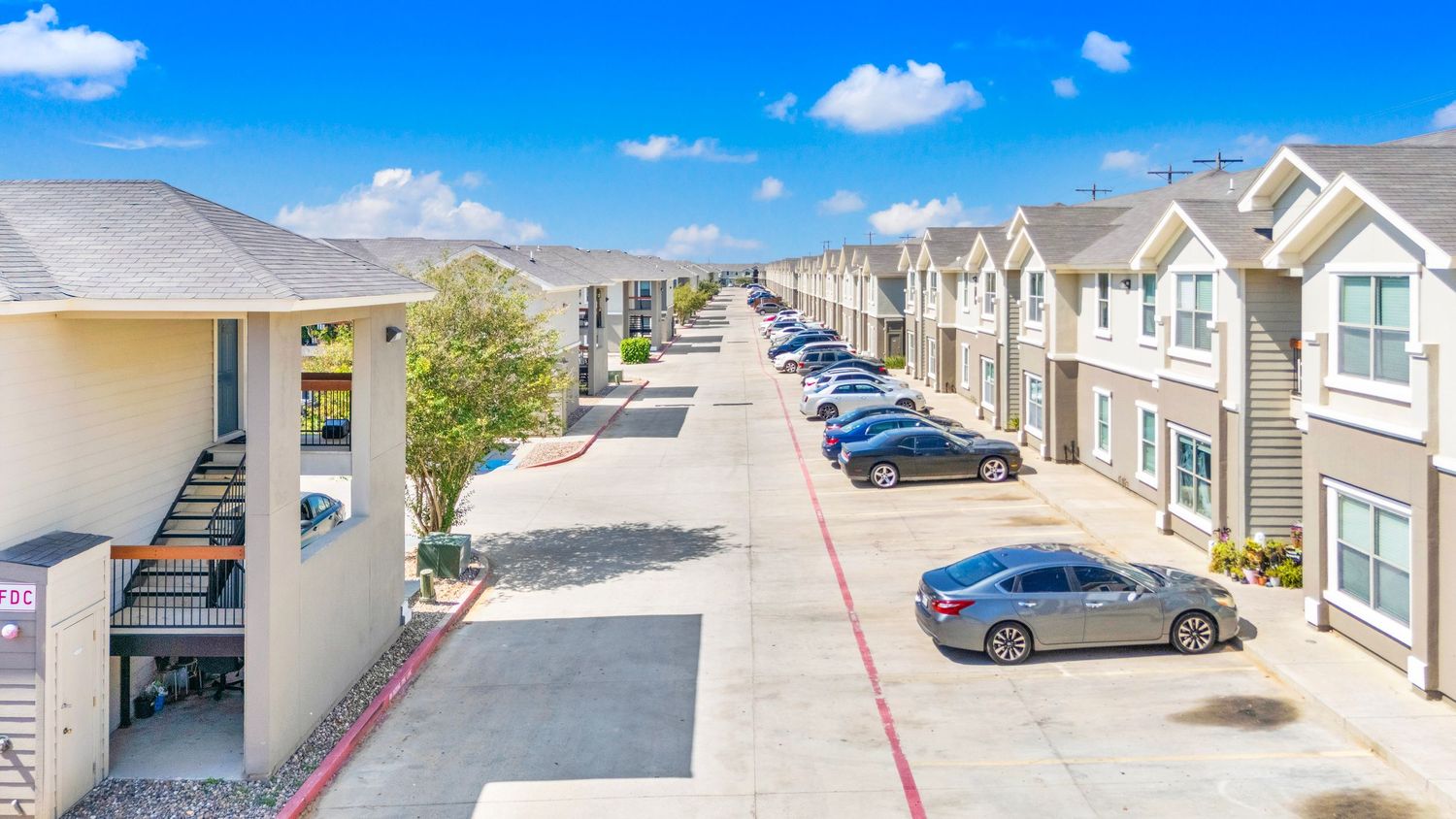 Panoramic view of modern residential apartment buildings with parking lots under bright blue sky.