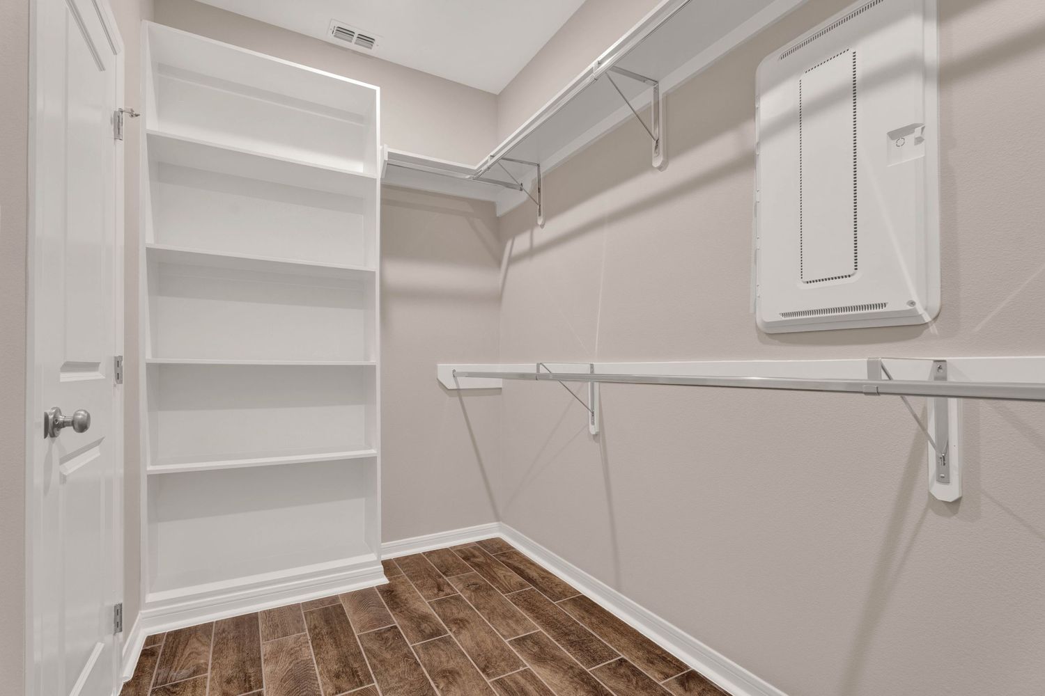 Spacious walk-in closet with white wire shelving, built-in cabinets, and dark hardwood-style flooring.