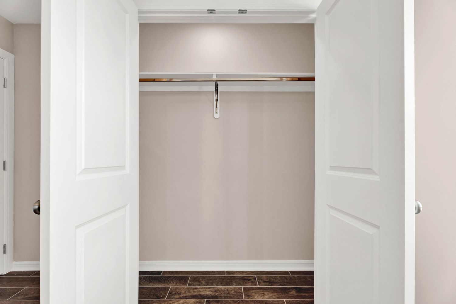 Open double-door closet with a single hanging rod and dark tile flooring in a neutral-toned room.
