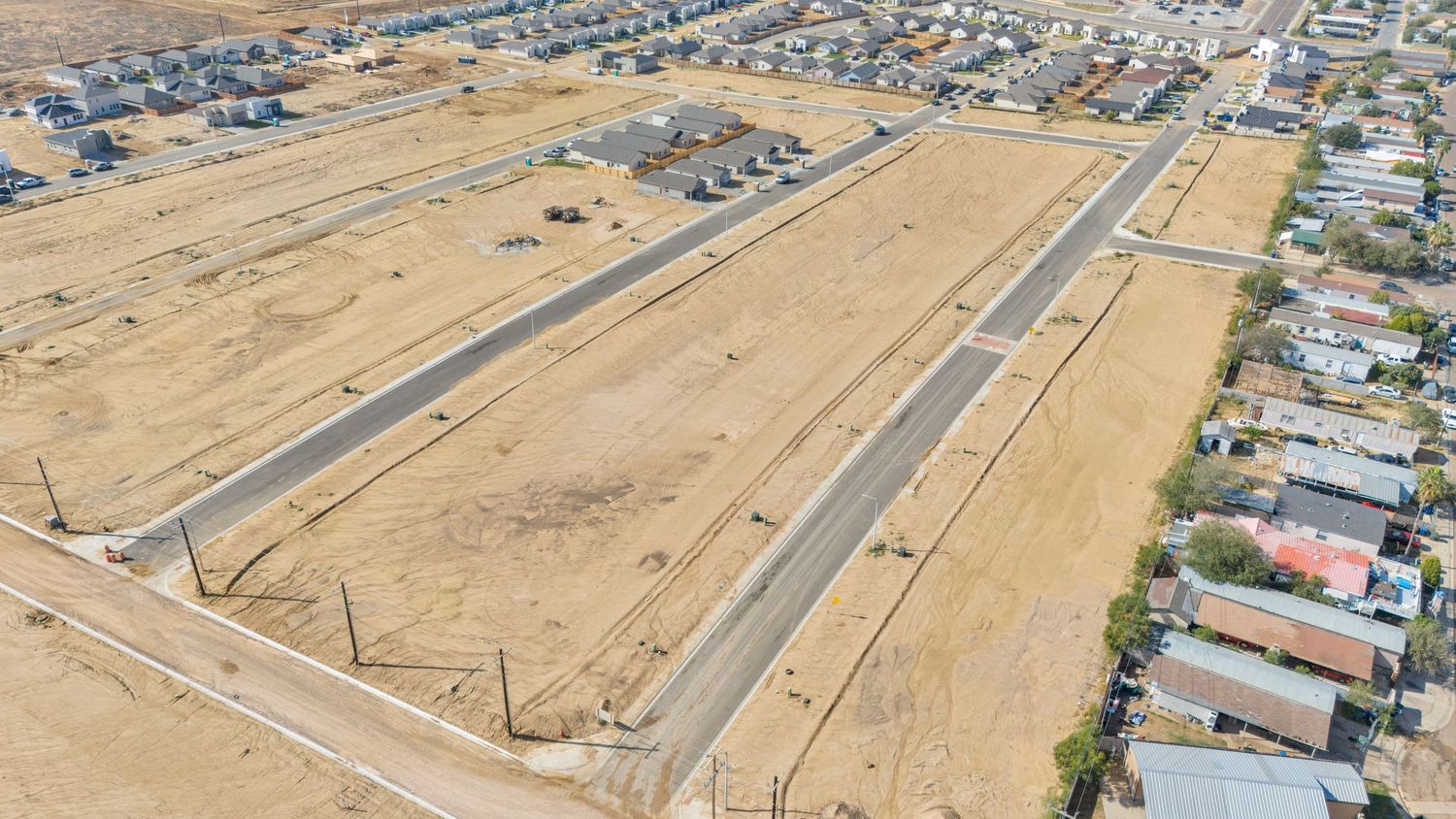 Aerial panoramic view of suburban housing development next to dry agricultural fields in a desert landscape.