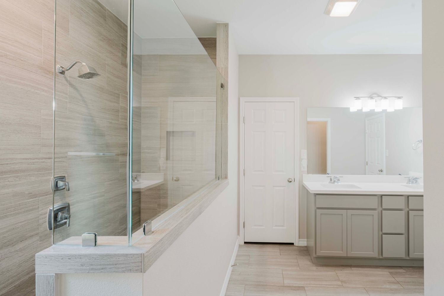 Modern bathroom featuring glass shower enclosure, wood-look tile, and gray double vanity with white countertop.