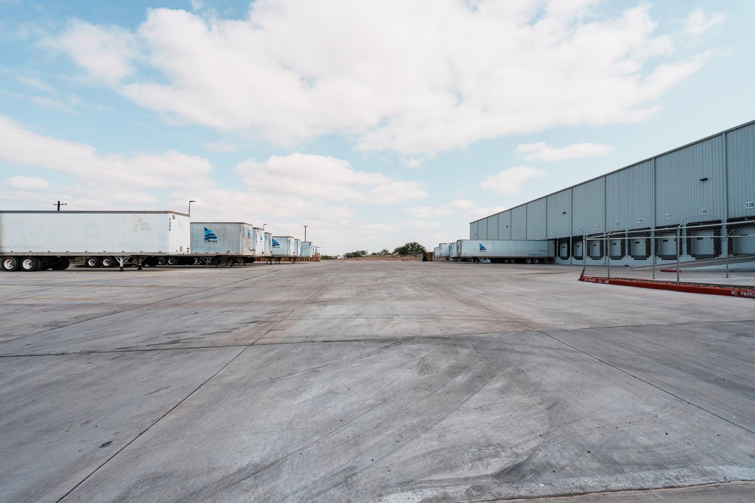 Large empty concrete loading dock area outside industrial warehouse buildings under blue sky with white clouds.