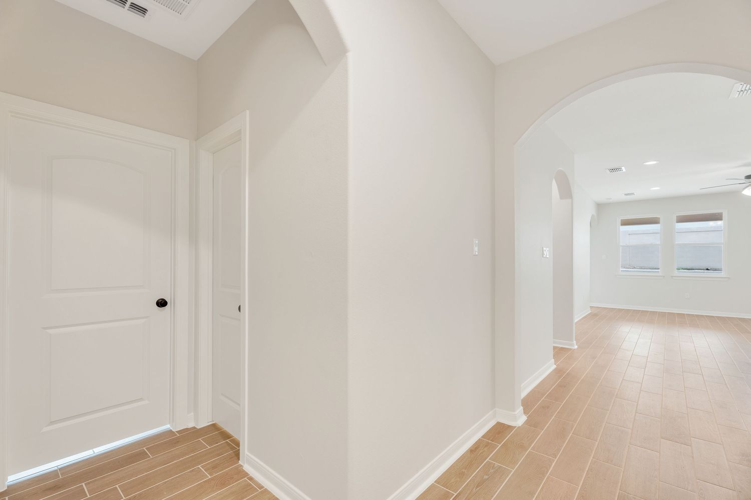 Interior hallway view of a modern home with white walls and baseboards showing multiple doorways and natural lighting.