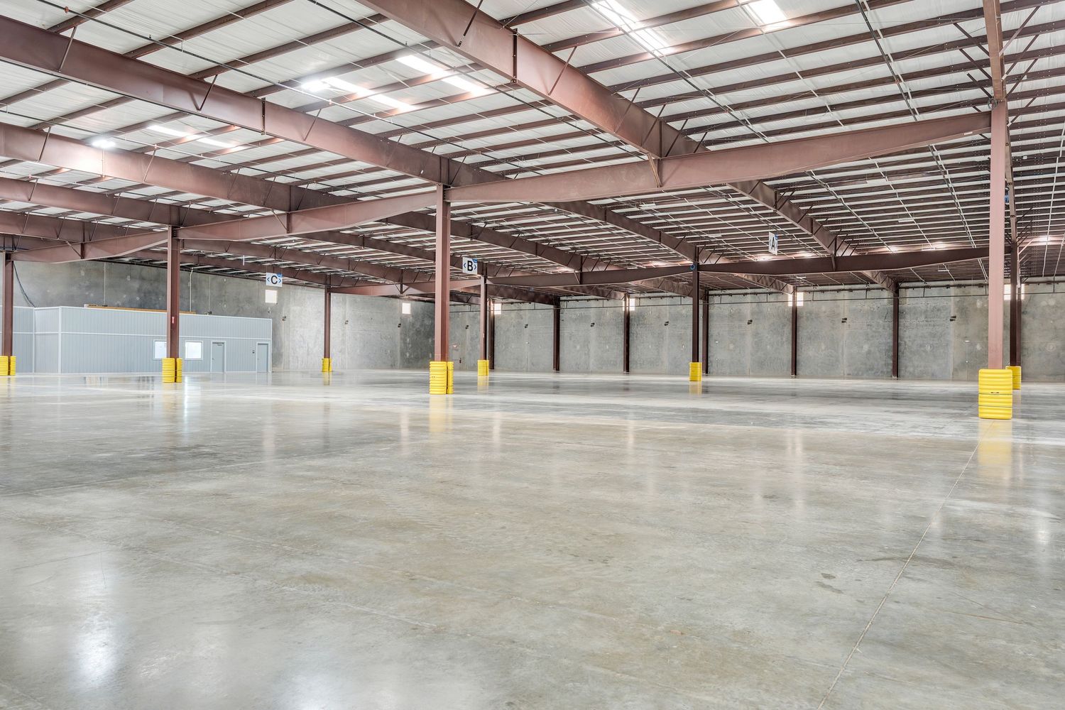 Large empty warehouse interior with polished concrete floors, exposed ceiling, and yellow support columns.