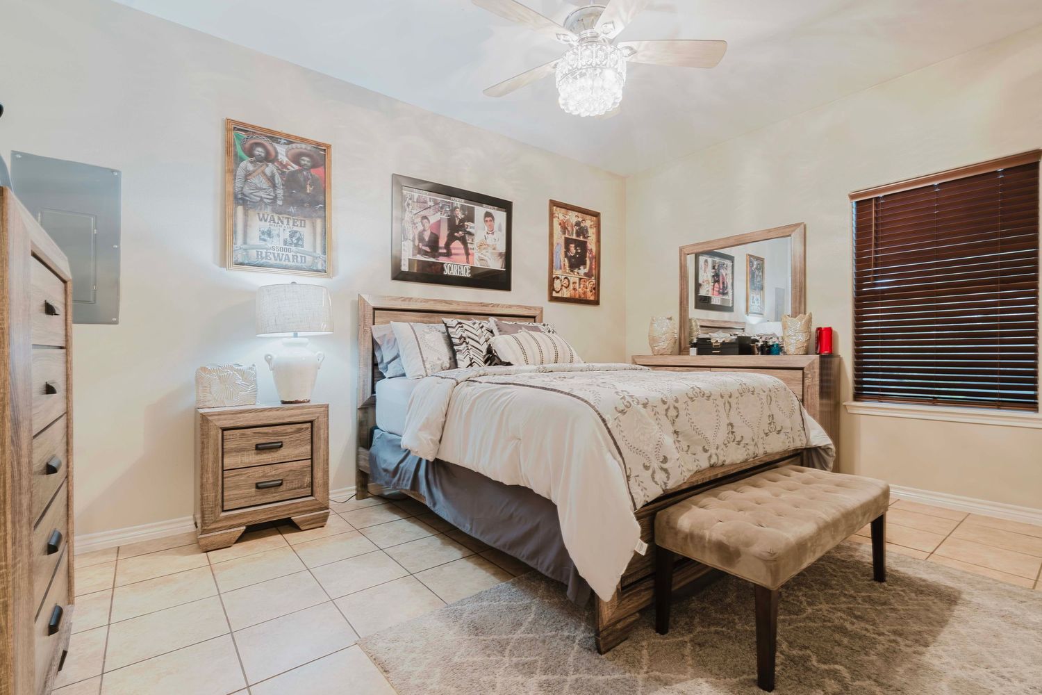 Elegant master bedroom with beige walls, tiled floors, bench seating, and framed artwork above the queen-sized bed.