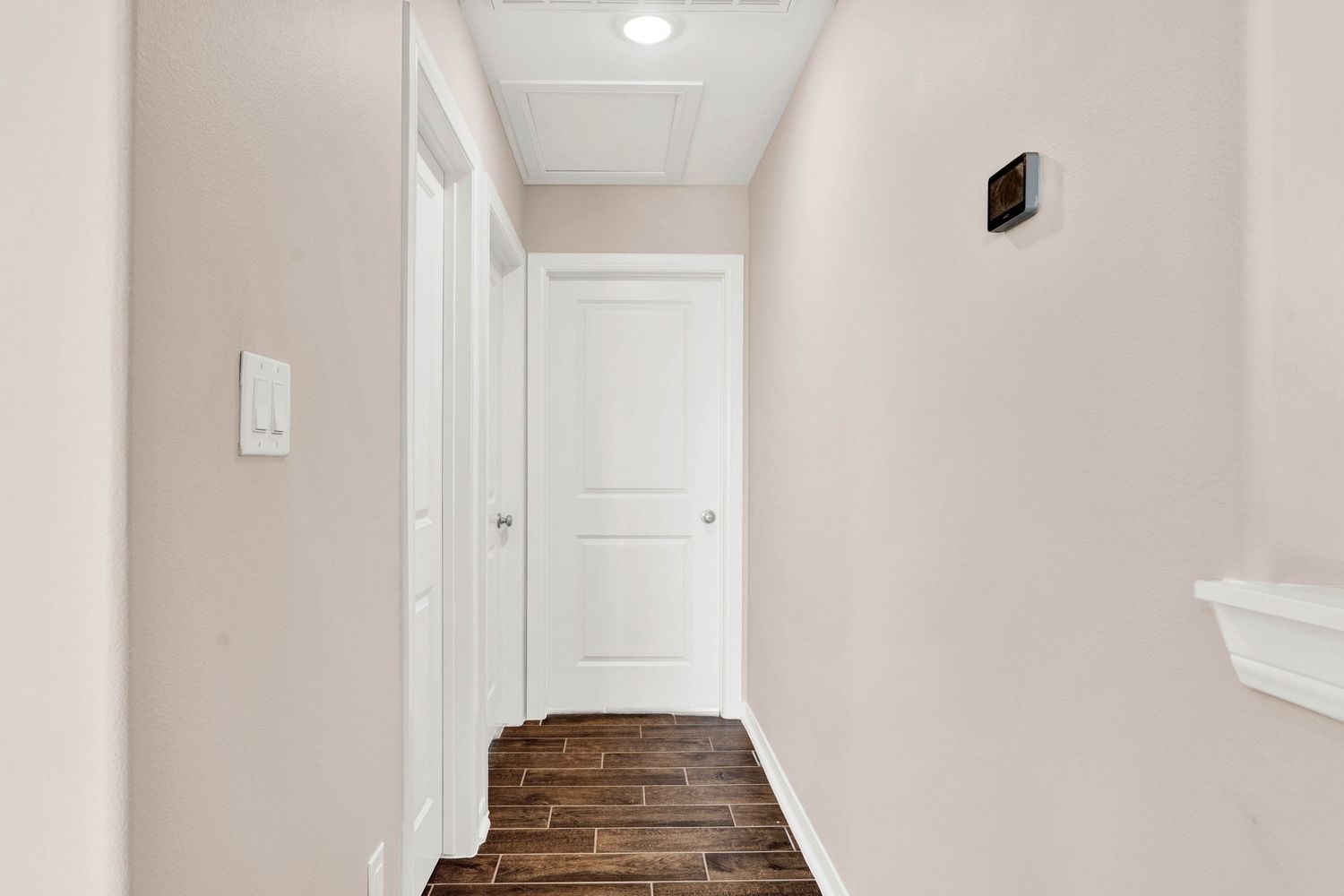 Narrow hallway with dark wood-look tile floors, white walls, white panel door, and a wall-mounted thermostat.