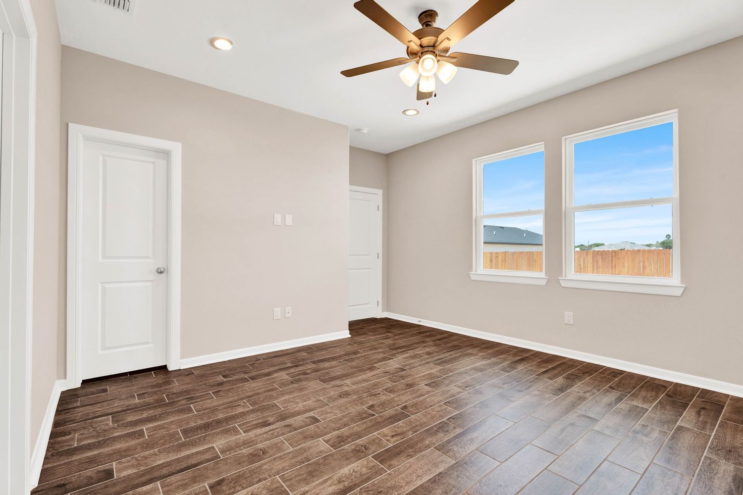 Bright empty room with dark hardwood floors, ceiling fan, neutral walls, and a window with natural light.