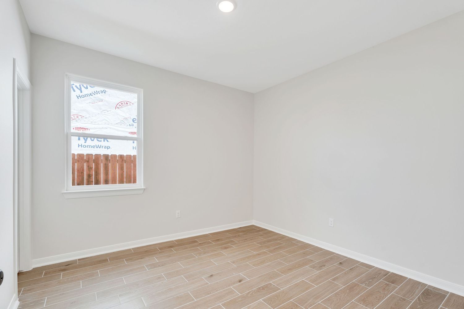 Modern white bedroom with light hardwood floors, recessed lighting, and large windows providing natural illumination.