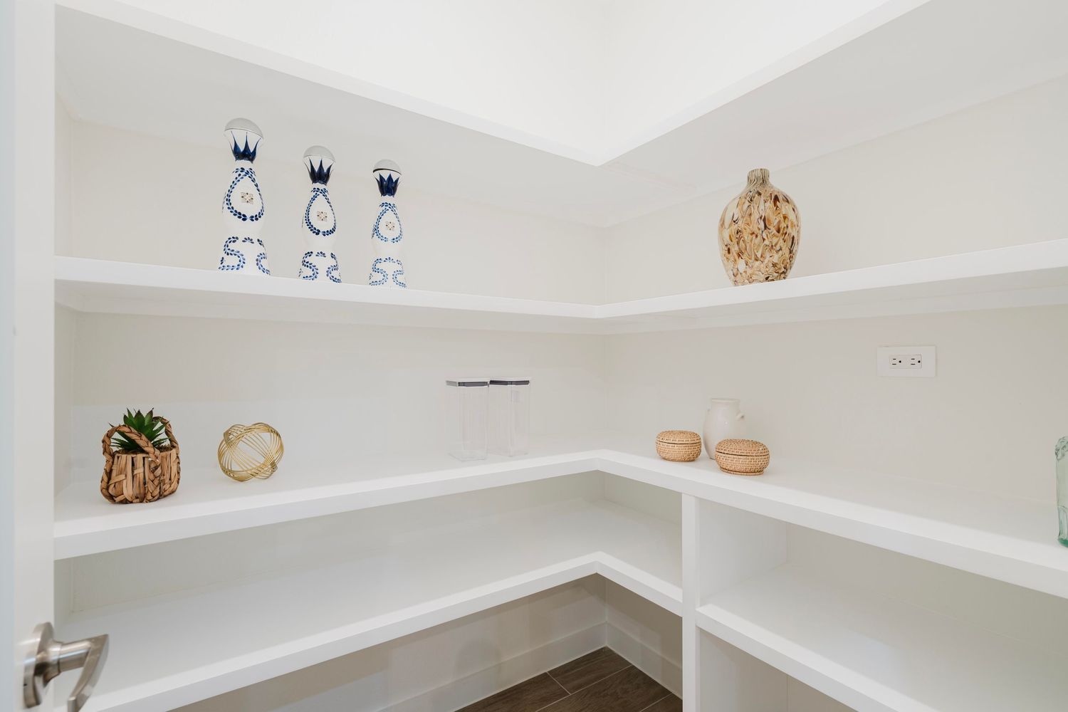 Corner pantry with white shelving displaying decorative bottles and woven storage baskets.