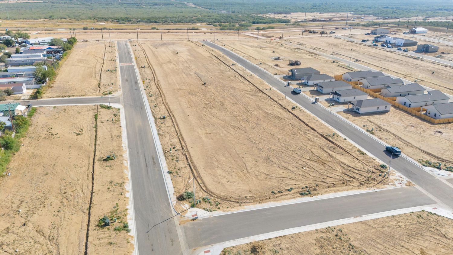 Aerial panoramic view of a newly developed residential subdivision with paved roads and empty lots in a desert landscape.