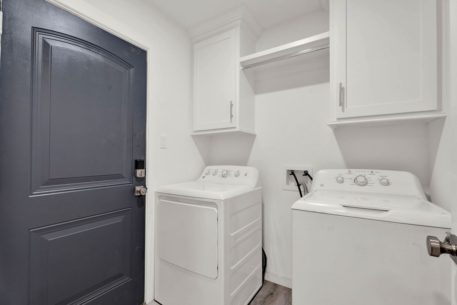 Laundry room with white washer and dryer, upper cabinets, and dark entry door.