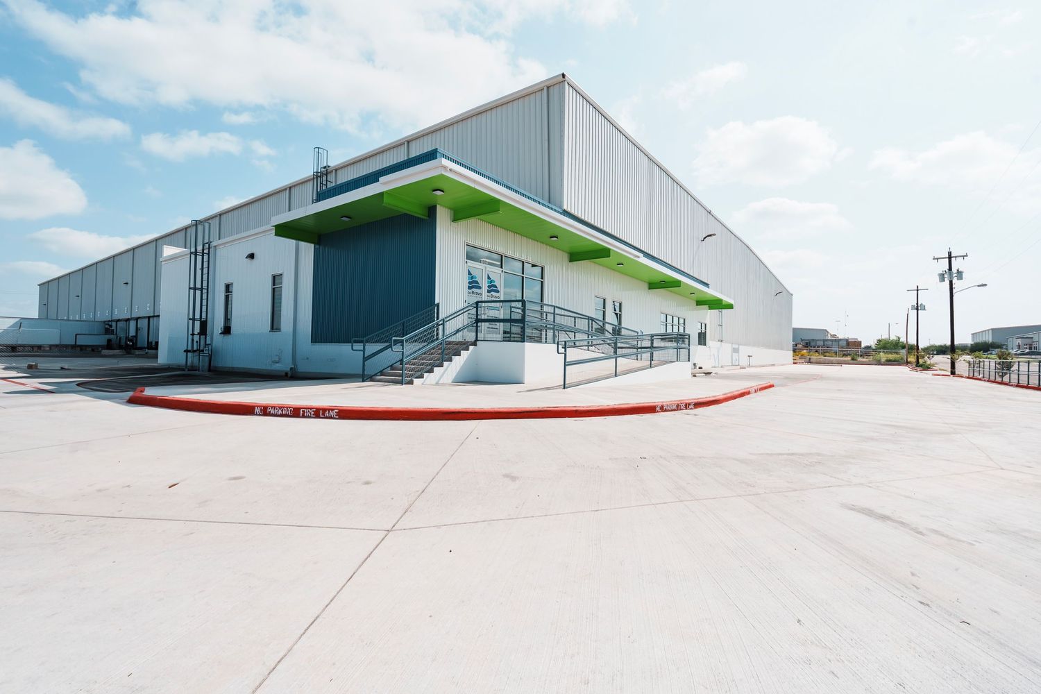 Modern industrial warehouse building exterior with green accent canopy and concrete loading dock area.