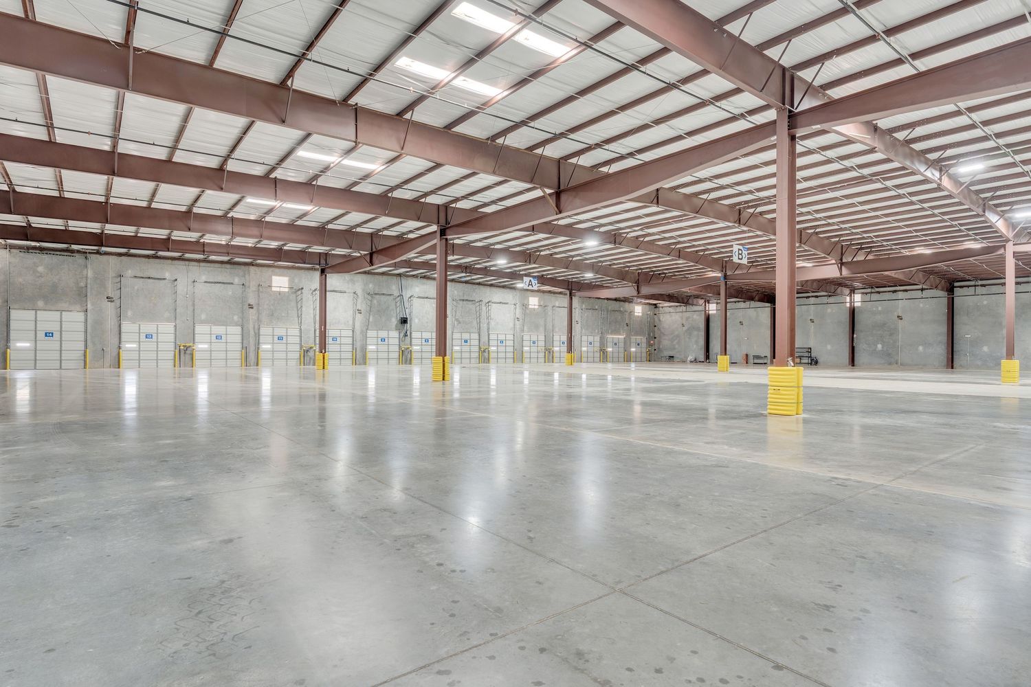 Large empty industrial warehouse interior with concrete floor and metal roof structure shows expansive storage space.