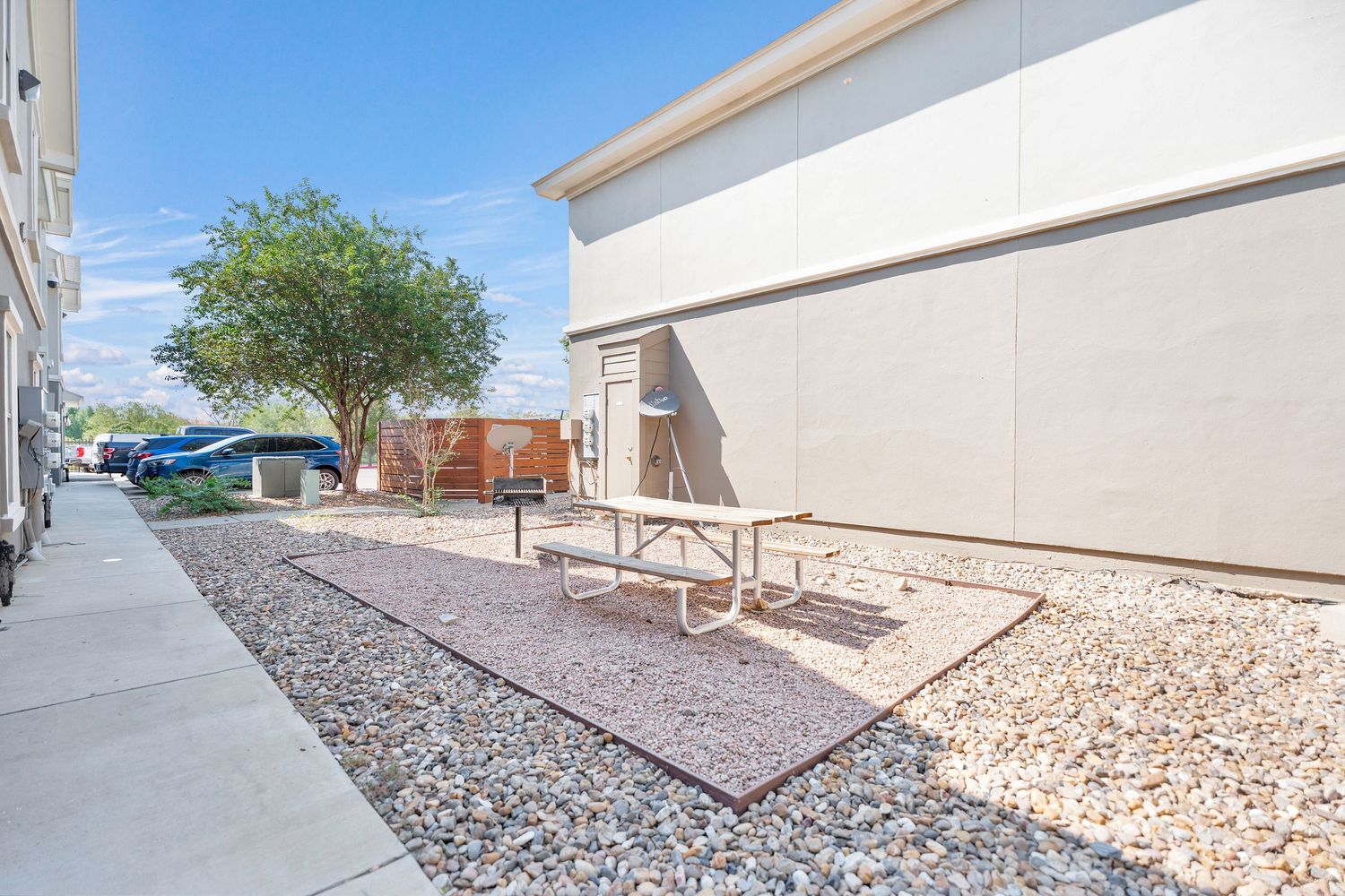 A gravel landscaped side yard with benches between white buildings under a blue sky.