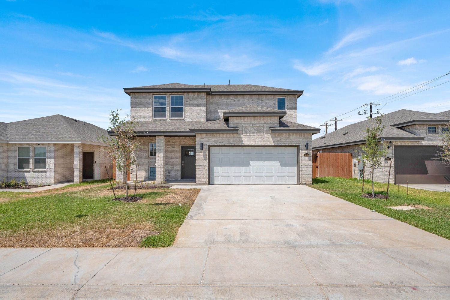 Two-story brick home with two-car garage, concrete driveway, and manicured lawn under a bright blue sky.