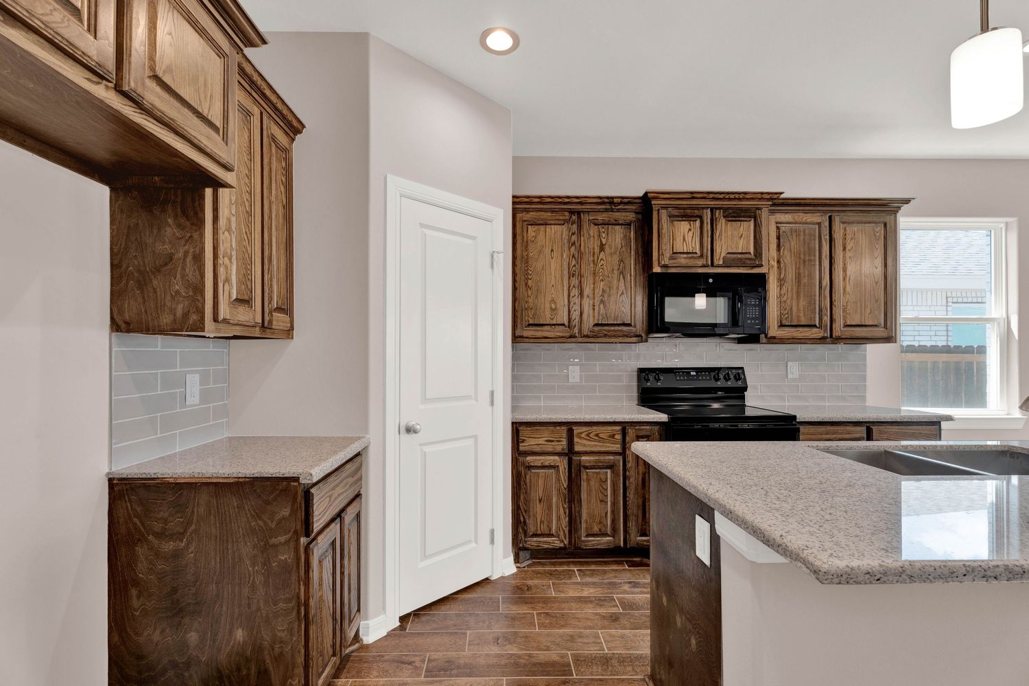Modern kitchen with dark wood cabinets, granite countertops, black appliances, and subway tile backsplash.
