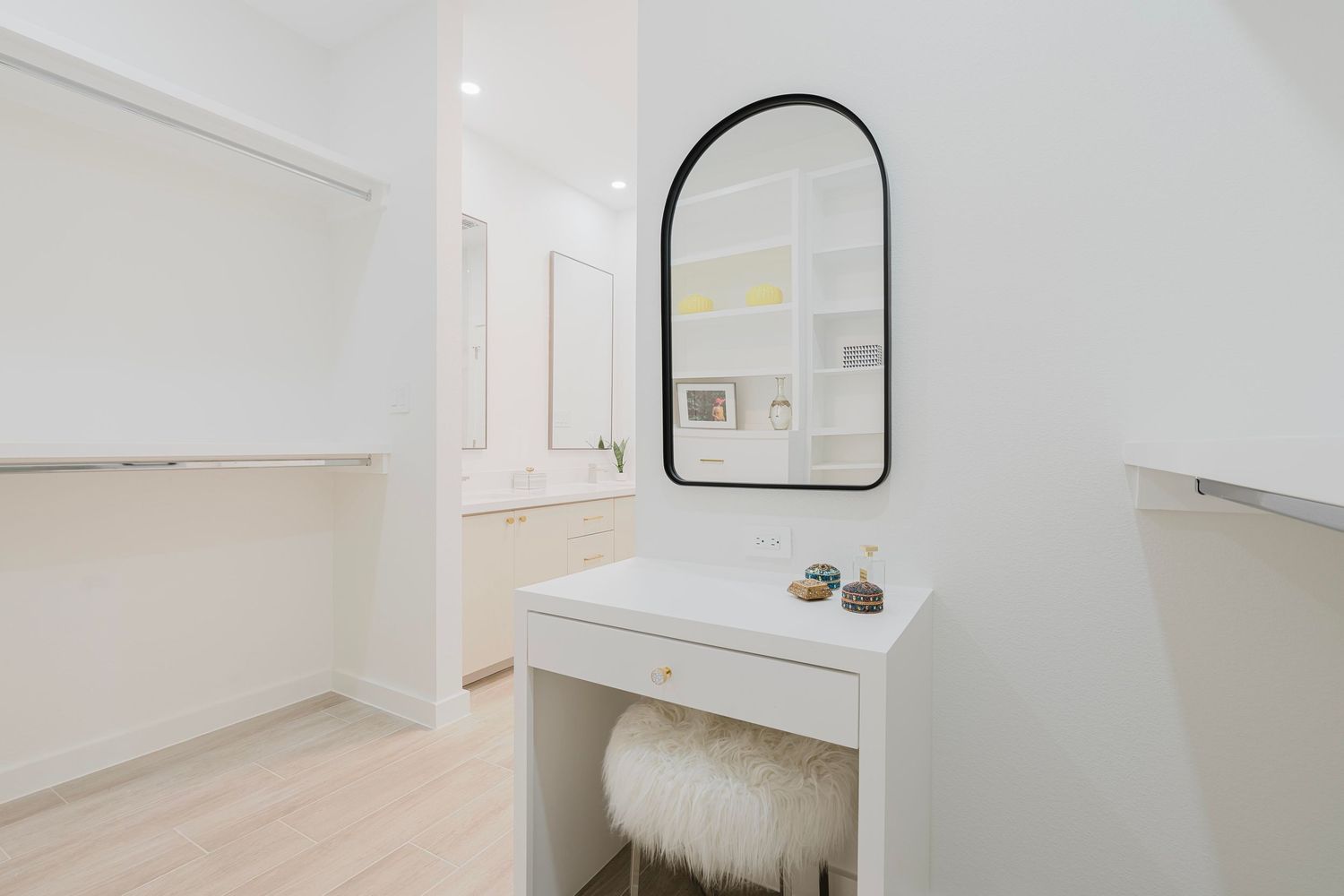 White dressing table with plush faux fur stool and arched black-framed mirror.