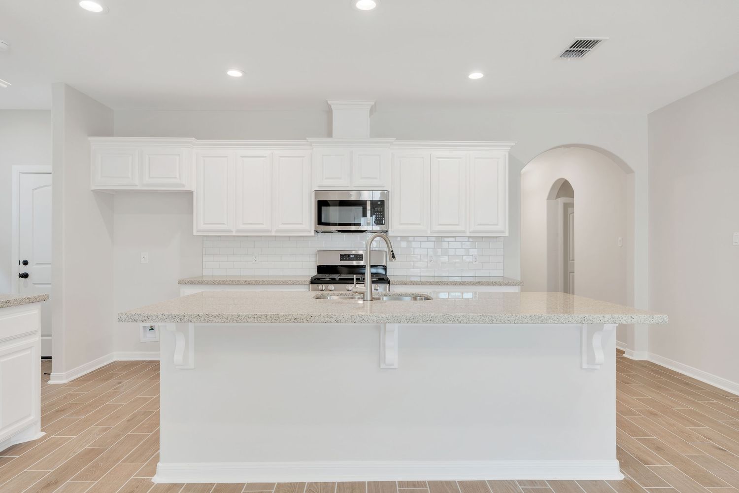 Modern white kitchen with quartz countertops, hardwood floors, and recessed lighting in an open concept layout.