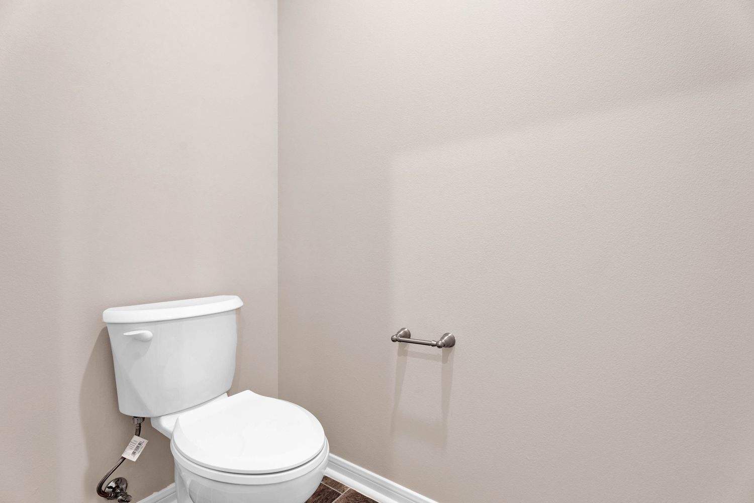 Clean white toilet in a small half bathroom with neutral beige walls and a chrome towel bar.
