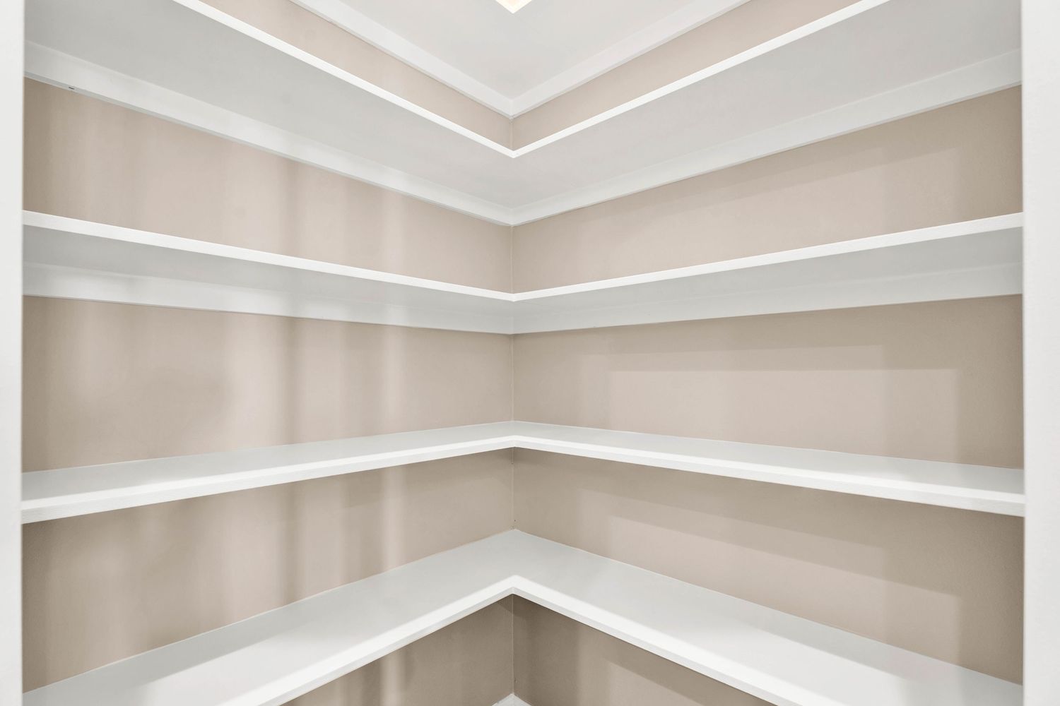 Empty walk-in pantry with white corner shelving and neutral striped wallpaper in a modern home.