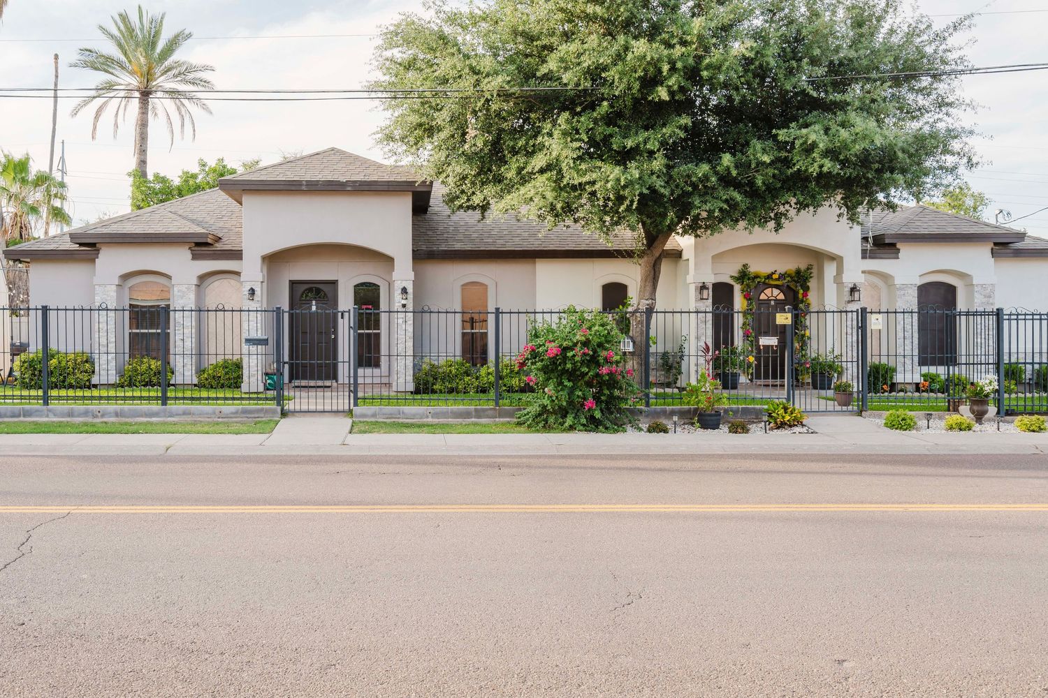 Spanish style residential property with gated entrance featuring palm trees and lush landscaping along a suburban street.