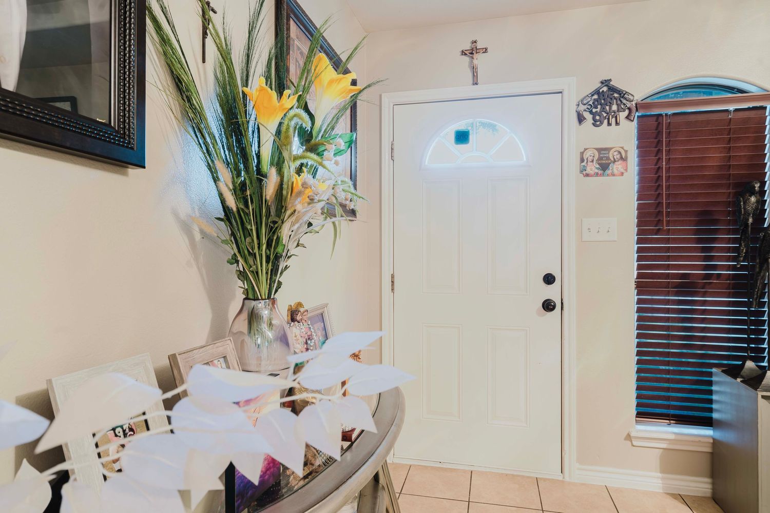 A bright entryway features a white door, tile flooring, and a decorative vase with yellow flowers on a side table.