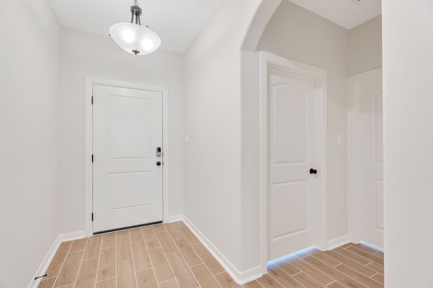 Modern white hallway with hardwood flooring, recessed lighting and multiple interior doors leading to different rooms.