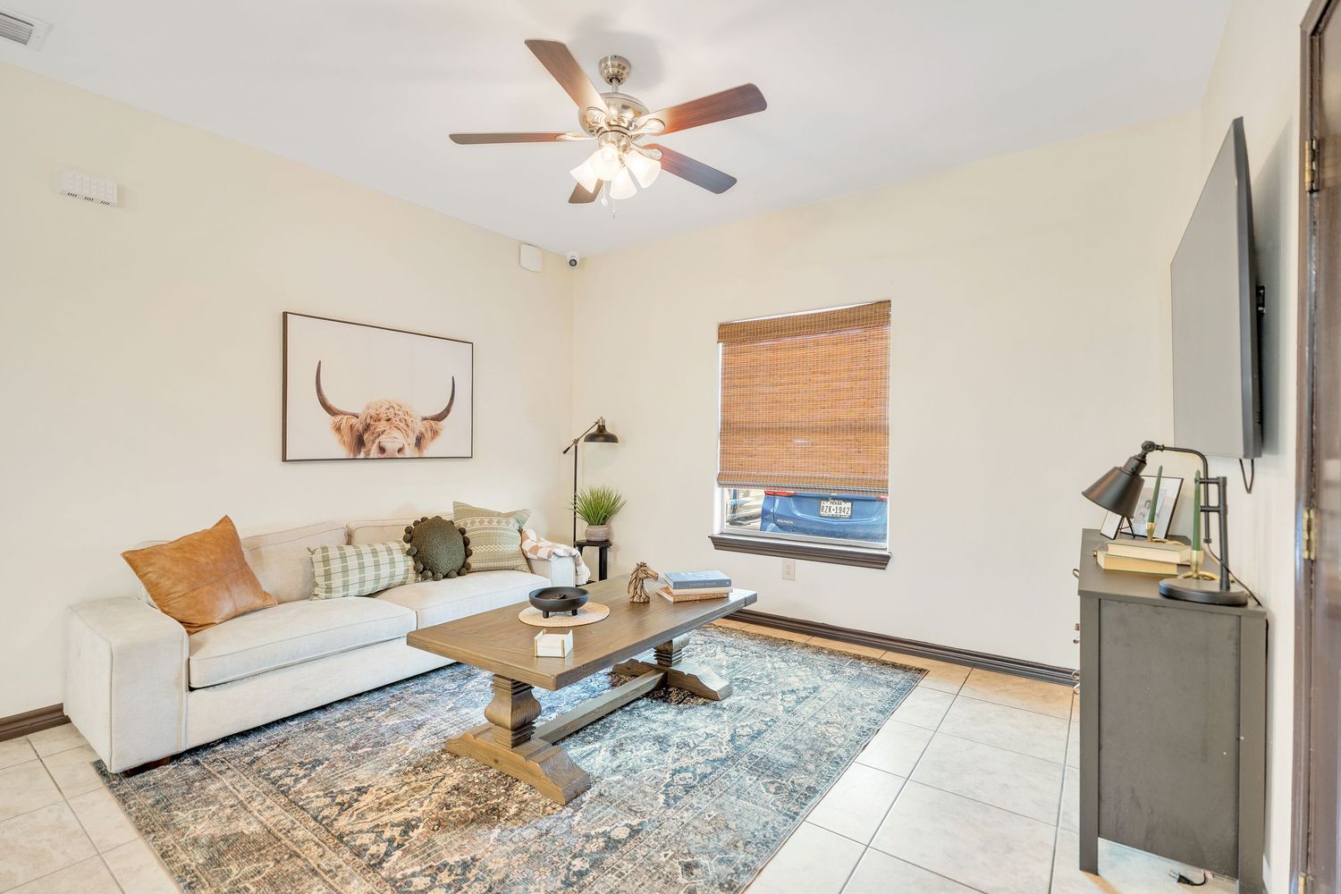 Spacious bedroom with ceiling fan, hardwood floors, and light blue area rug under natural lighting.