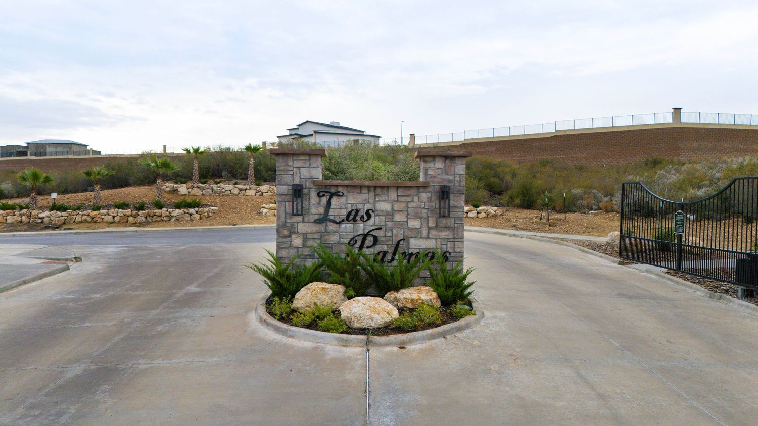 A panoramic view of a gated entrance to a residential community with stone pillars and landscaped roundabout.