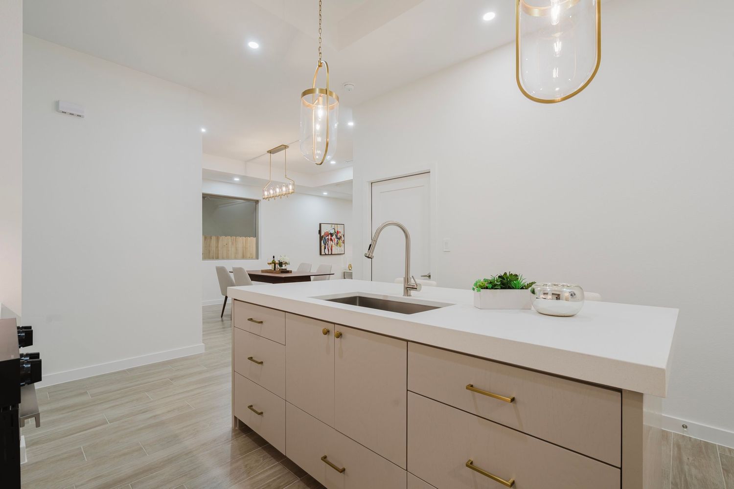 Contemporary kitchen featuring beige cabinets, pendant lights, and white countertops with gold hardware.