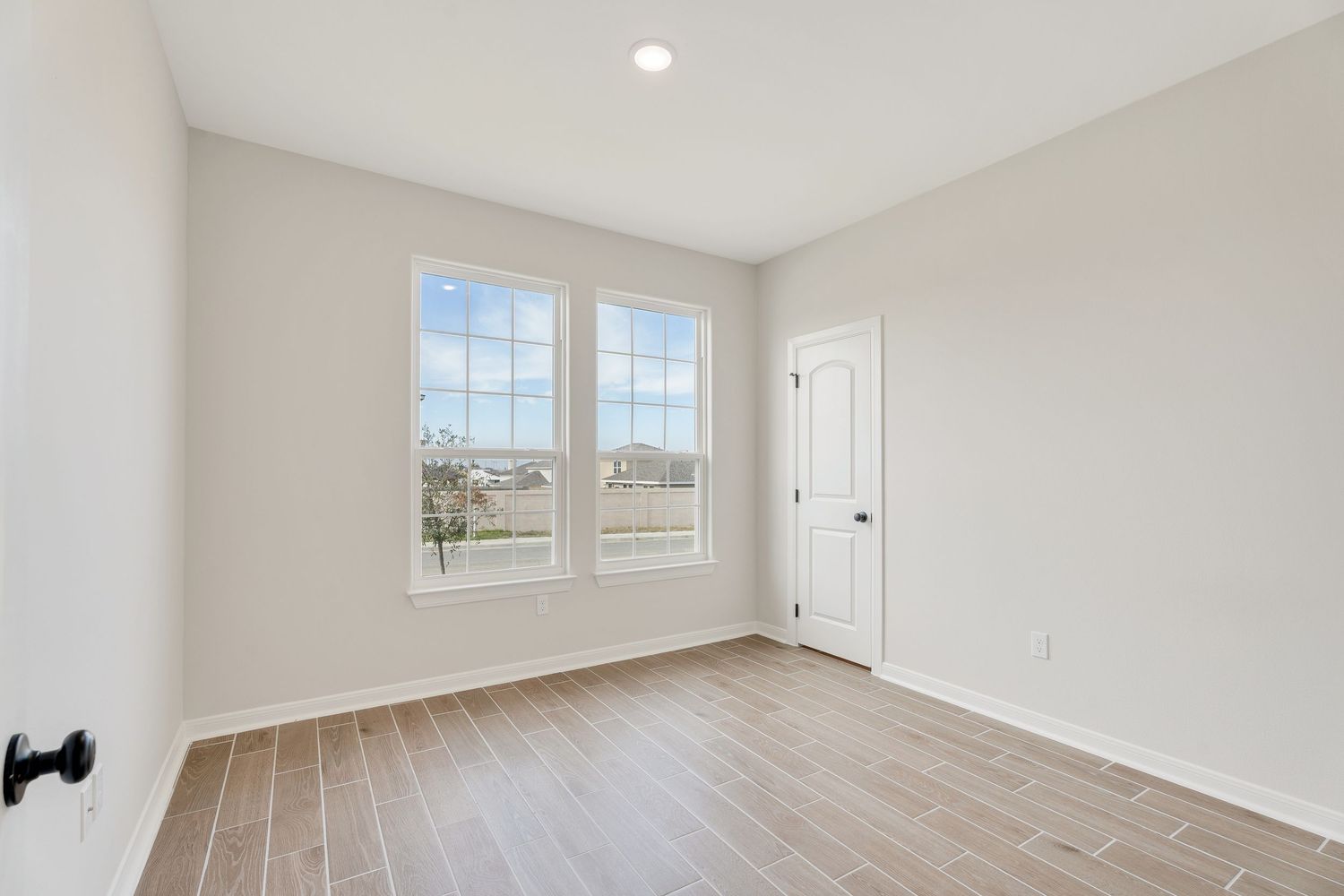 Modern empty bedroom with light hardwood floors, white walls, and large windows letting in natural light.