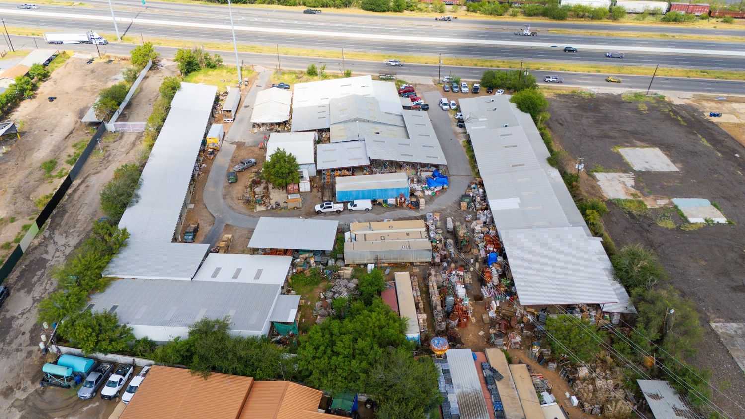 Aerial view of warehouses and commercial buildings with surrounding dirt lots and parked vehicles.