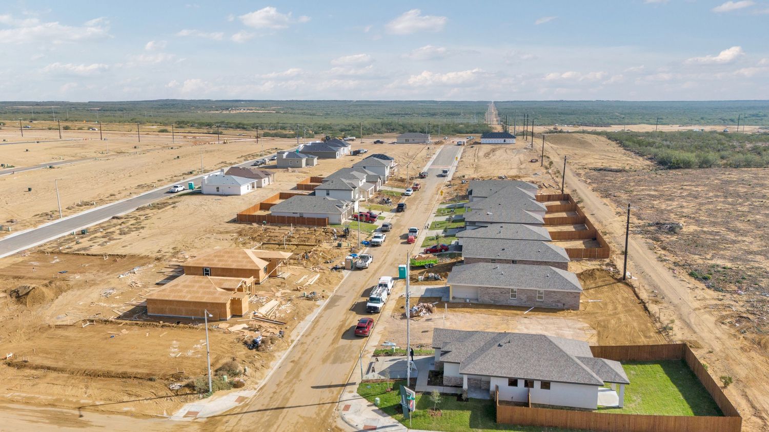 Aerial panoramic view of a construction site with multiple buildings and roads in development under a blue sky.