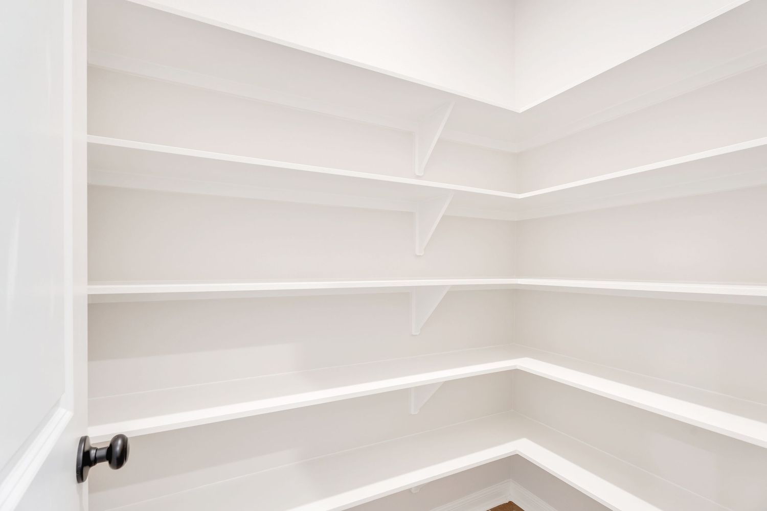 A modern white walk-in closet with built-in shelving and hanging rods features elegant crown molding and recessed lighting.