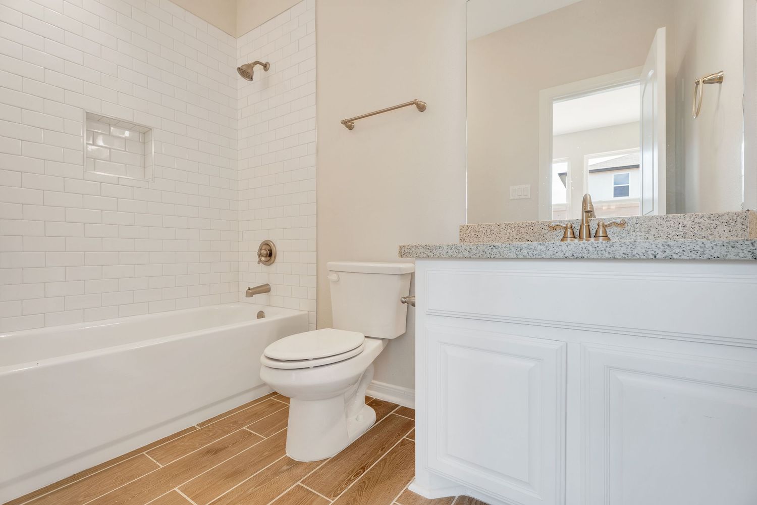 A modern white bathroom interior with hardwood floors, granite countertops, and bright lighting fixtures.