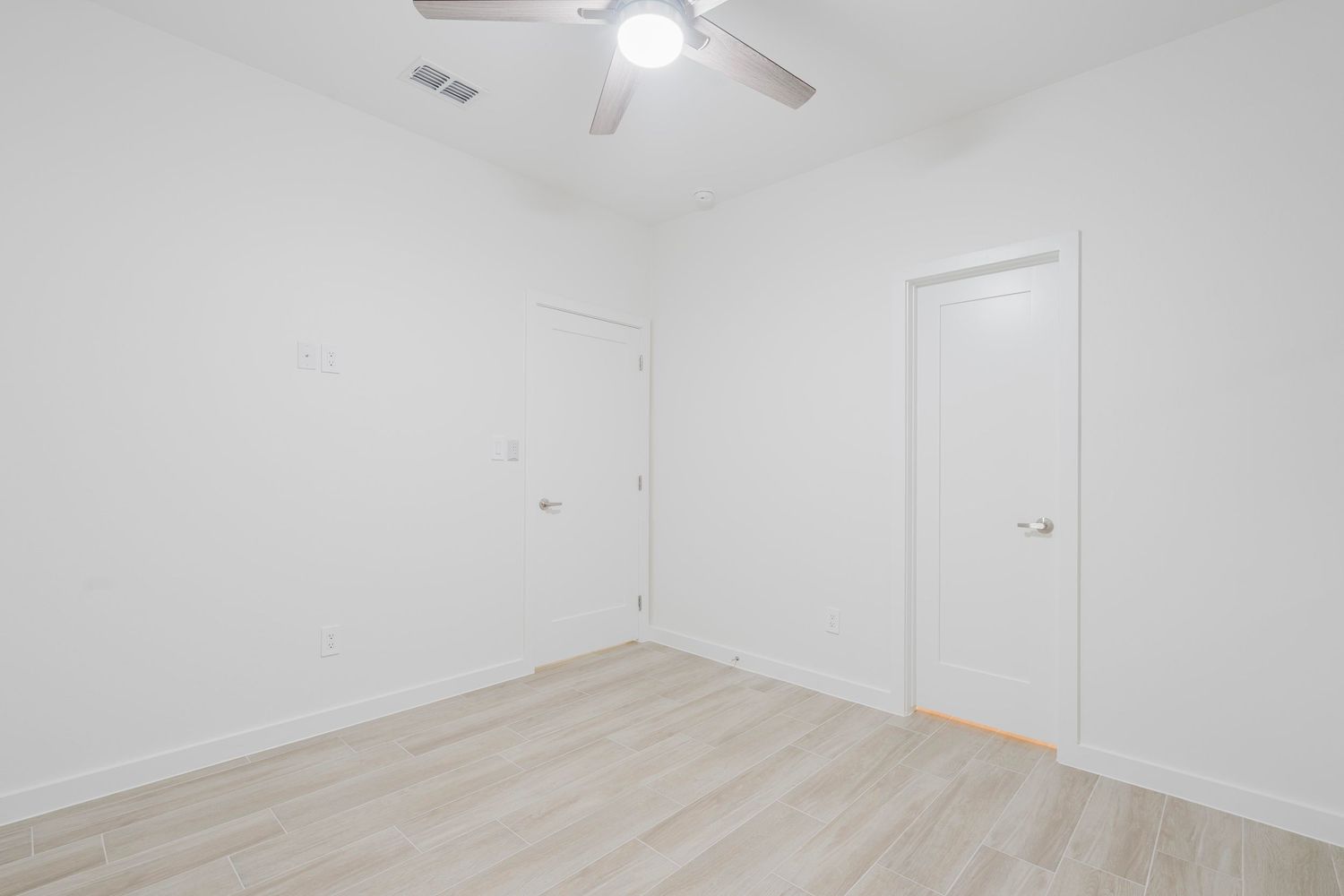 Empty room with white walls, ceiling fan, and light wood flooring.