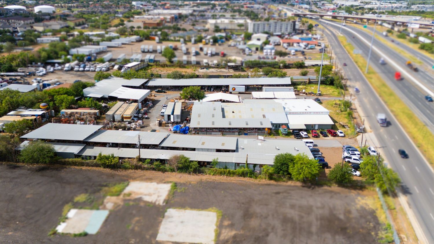 Aerial panorama of industrial and commercial buildings along highway with parked vehicles and storage facilities.