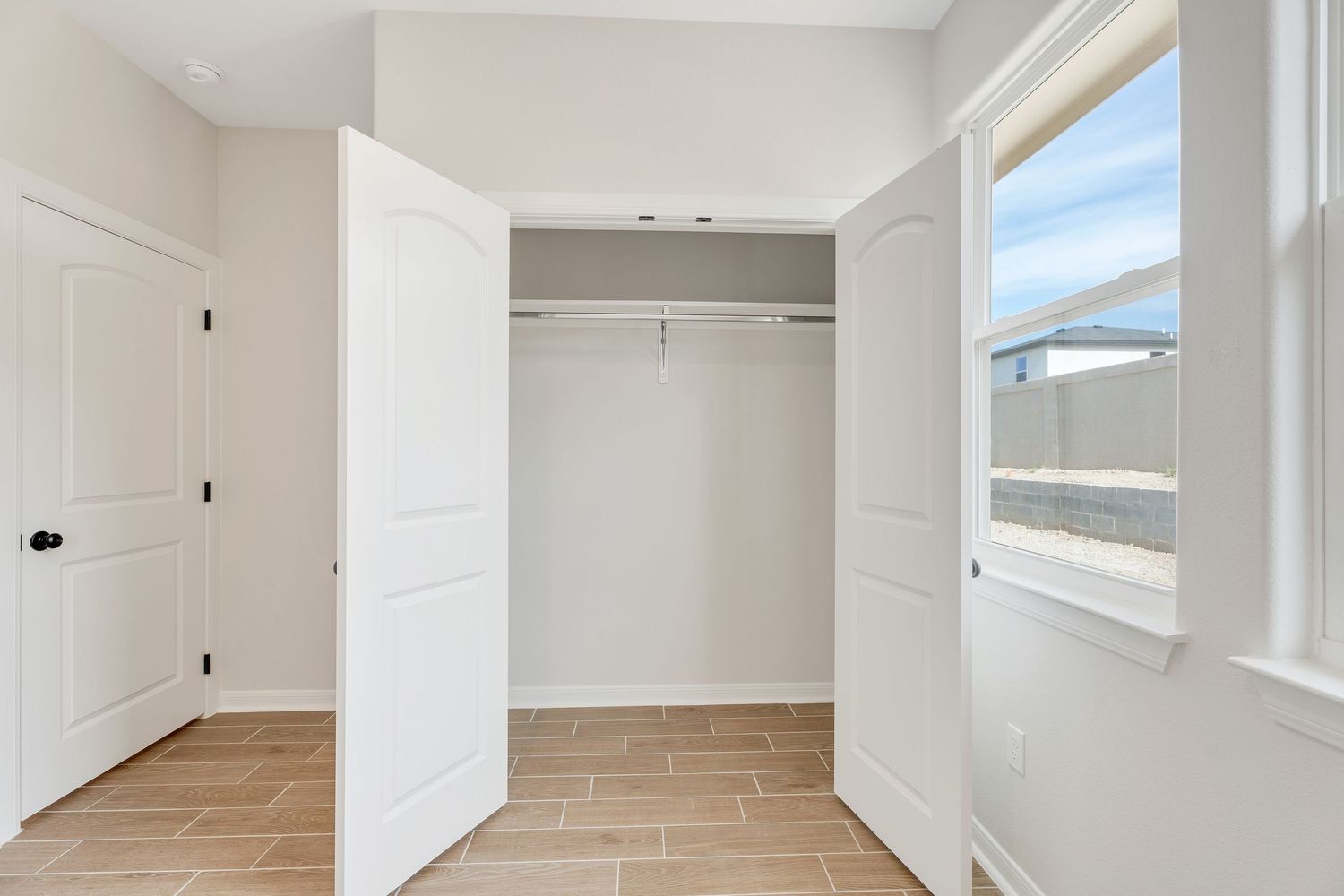 A bright, modern empty room with white walls, hardwood floors, and large windows letting in natural light.