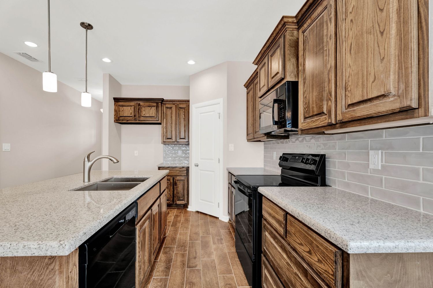 Modern kitchen with dark wood cabinets, granite countertops, black appliances, subway tile backsplash, and hardwood floors.